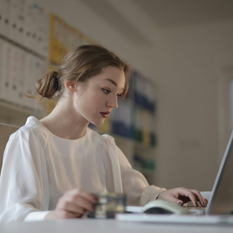 Focused young woman working remotely on a laptop in a modern office.