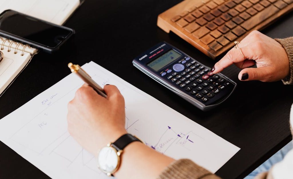 Close-up of hands working with a calculator and notebook on a desk, analyzing documents.