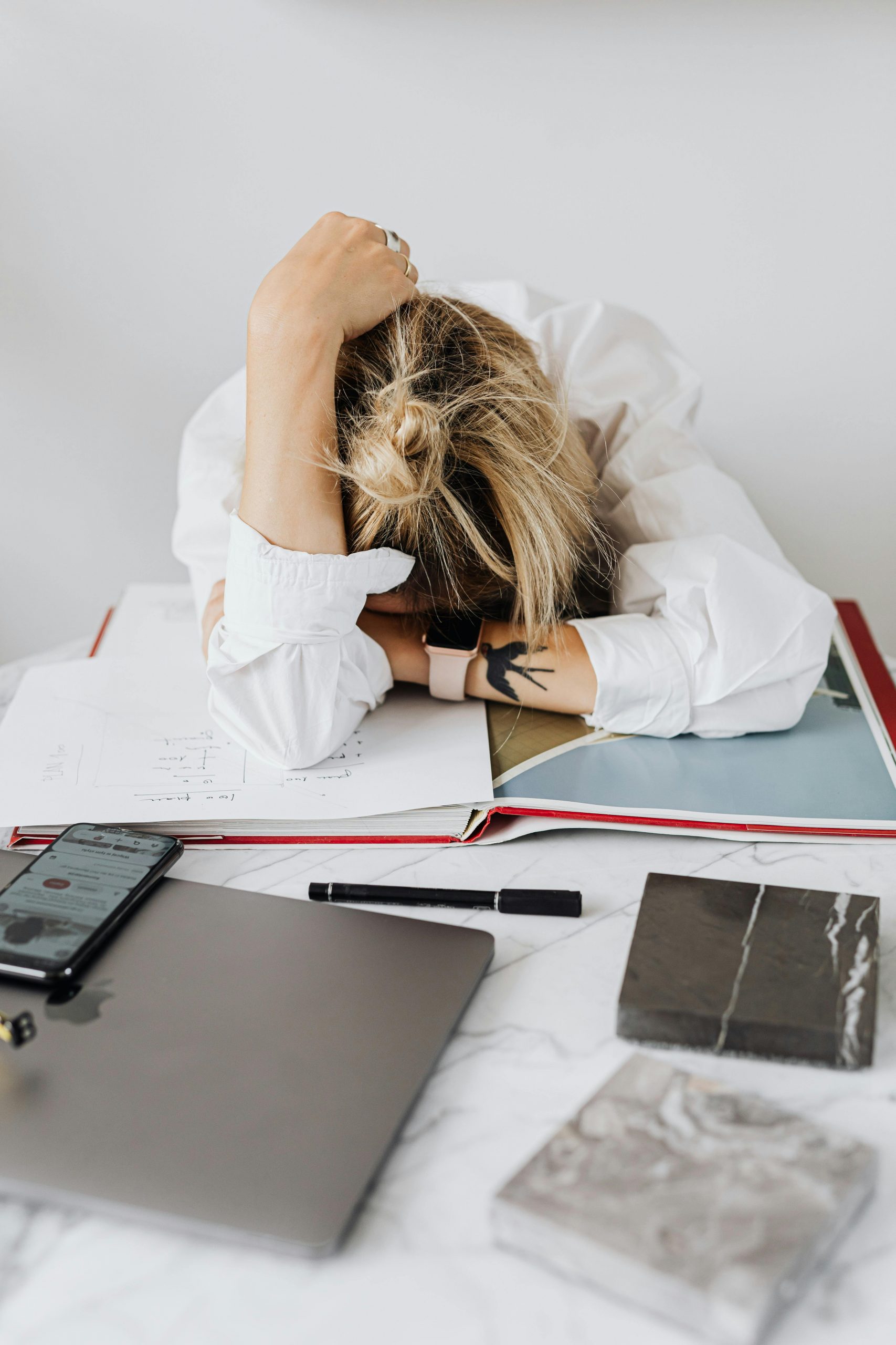 Overwhelmed woman resting head on desk with laptop and papers in home office.