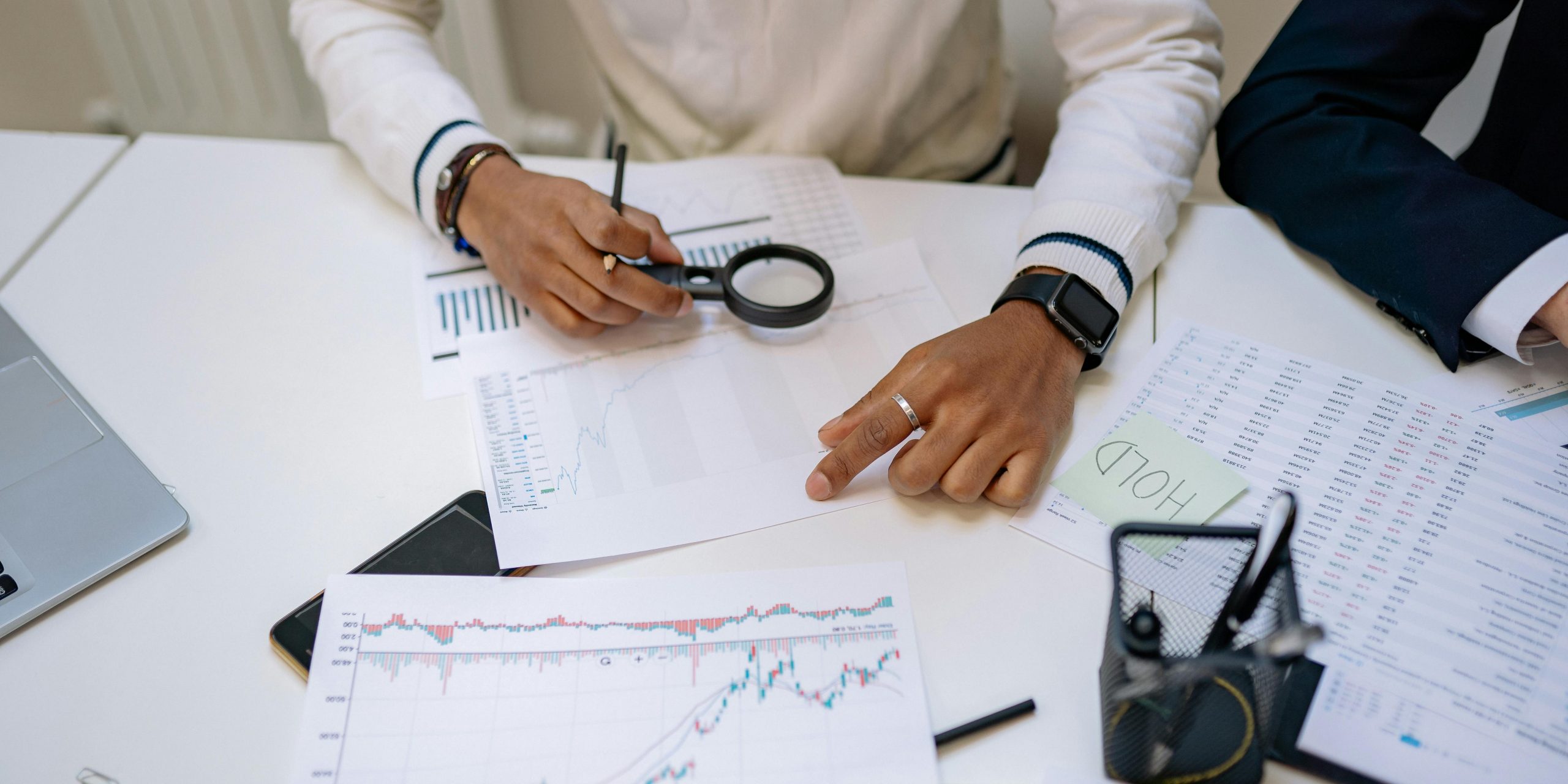 Business professionals reviewing charts with a magnifying glass in an office setting.